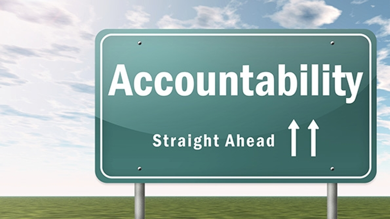 Green highway sign reading "Accountability Straight Ahead" with upward arrows against cloudy sky and grass field below.